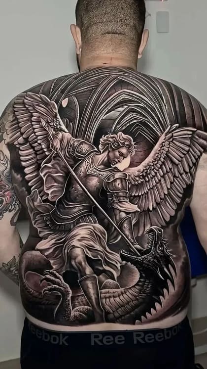Tatuagem de fechamento de costas em realismo preto e cinza, retratando Arcanjo Miguel em armadura com lança, derrotando um dragão, com fundo de arquitetura gótica.