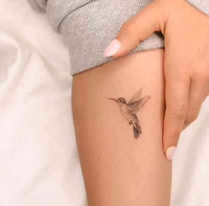 Tatuagem de beija-flor em estilo fineline no braço, com detalhes delicados em preto e cinza.