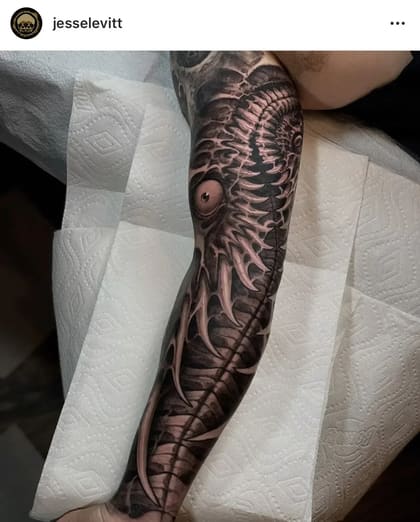 Tatuagem bio-orgânica em preto e cinza no braço, com um olho realista e estruturas ósseas detalhadas.
