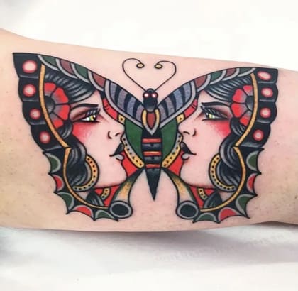 Tatuagem Old School de borboleta com duas faces femininas, cores vibrantes e contornos marcados.