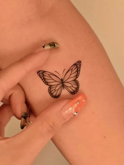 Tatuagem de borboleta em estilo fineline no braço, preta e delicada.