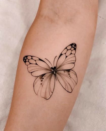 Tatuagem de borboleta em estilo fineline, preta e cinza, no antebraço de uma pessoa.