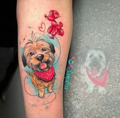 Tatuagem de cachorro feliz em estilo aquarela com bandana vermelha, balão de cachorro e corações, em um braço.