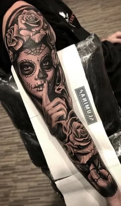 Tatuagem de manga completa estilo Chicano com Calavera Catrina, rosas e gesto de silêncio em preto e cinza.