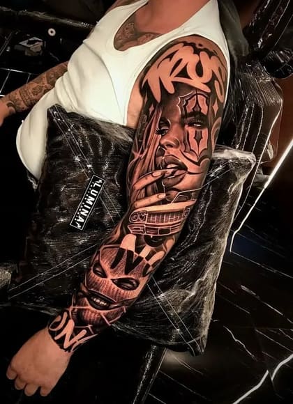 Tatuagem Chicano full sleeve em preto e cinza com rosto de mulher chola, carro lowrider e máscara, detalhada no braço de um homem.