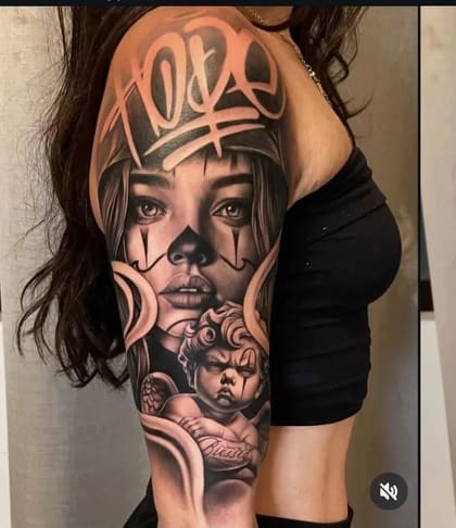Tatuagem Chicano em preto e cinza de mulher palhaça com bandana e querubim com lettering 'Blessed' no braço de uma mulher.