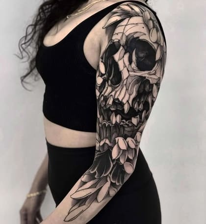 Tatuagem de braço completa estilo Blackwork com crânio detalhado e folhagens escuras em uma mulher.