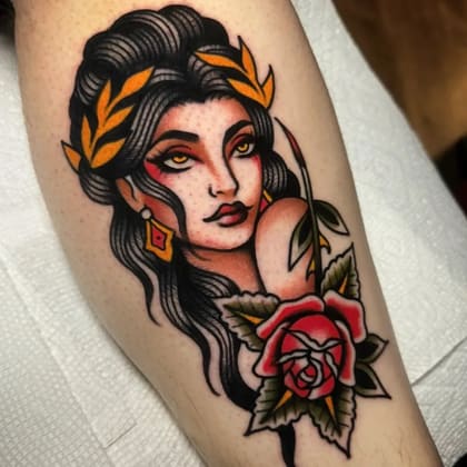 Tatuagem Old School colorida de uma mulher com coroa de louros e uma rosa vermelha no estilo tradicional.