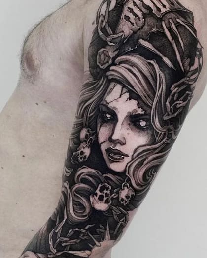 Tatuagem blackwork de deusa sombria com olhos brilhantes, caveiras e ossos no braço, estilo dark art.