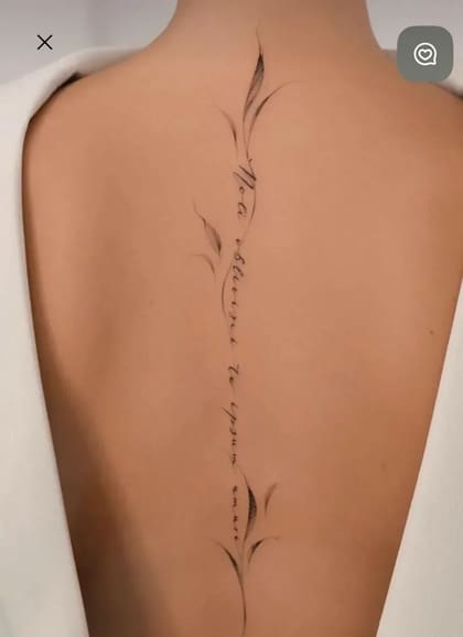 Tatuagem fineline delicada na coluna de uma mulher, com a frase em latim 'Non oblivisci te ipsum amare' e detalhes florais em preto.