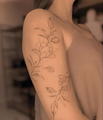 Tatuagem floral fineline delicada no braço de uma mulher, com ramos e flores em traço fino, estilo minimalista.