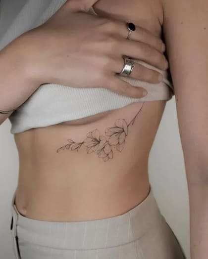 Tatuagem floral fineline delicada na costela de uma mulher, com traços finos e design minimalista.