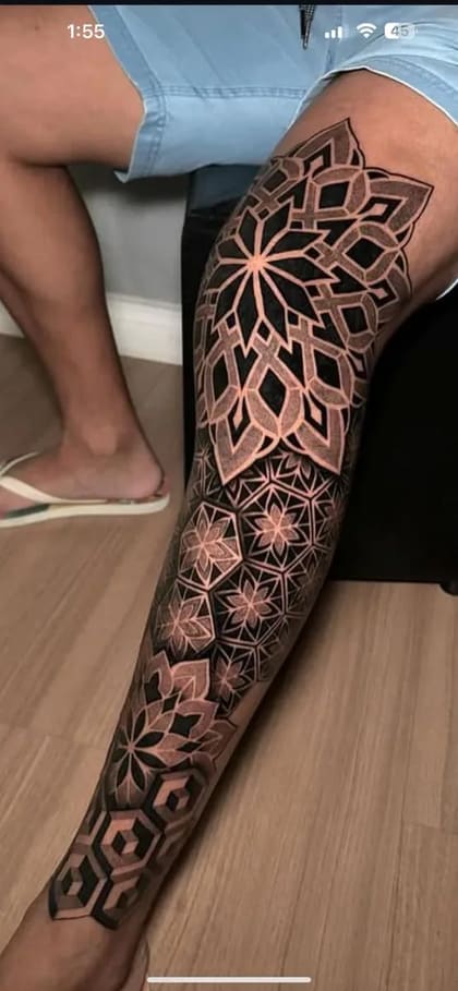 Tatuagem geométrica em pontilhismo cobrindo a perna de um homem, com padrões intrincados e simétricos em preto e cinza.