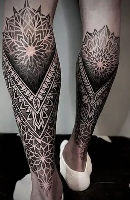 Tatuagem geométrica de pontilhismo nas pernas com padrões de mandala e ornamentos em preto e cinza.