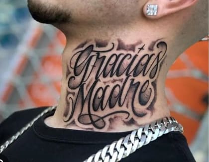 Tatuagem 'Gracias Madre' em estilo lettering chicano no pescoço de um homem, com sombreamento blackwork e detalhes de fumaça.