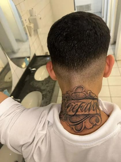 Tatuagem lettering 'Inefável' em preto e cinza na nuca de um homem, com detalhes ornamentais.