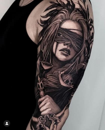 Tatuagem de Justiça Cega em estilo Blackwork no braço, com balança, espada e caveira, rica em detalhes e sombreamento.