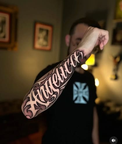 Tatuagem lettering Angelica estilo Chicano no antebraço masculino, com sombreado e contorno branco.
