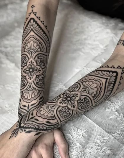Tatuagem mandala floral blackwork simétrica nos antebraços, com padrões ornamentais detalhados em preto.