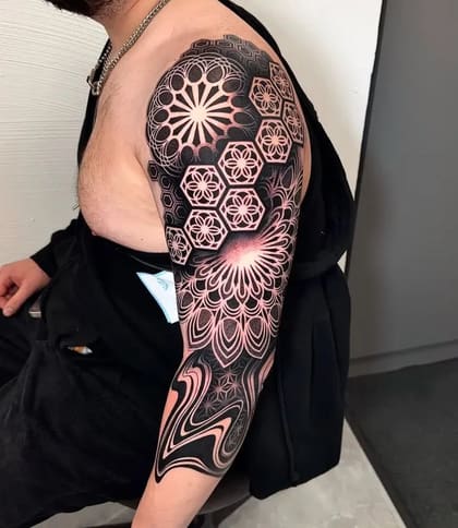 Tatuagem de manga geométrica blackwork com padrões abstratos e efeito de ilusão de ótica em braço masculino, feita no Brasil.