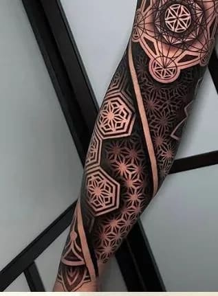 Tatuagem geométrica blackwork em manga completa, com padrões intrincados de geometria sagrada e mandalas no braço.
