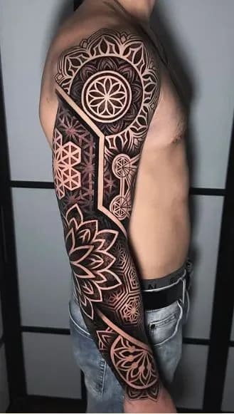 Tatuagem de manga geométrica blackwork com padrões de geometria sagrada e mandalas no braço de um homem.