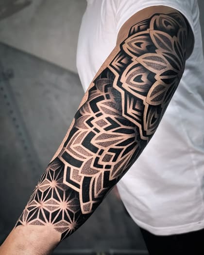 Tatuagem geométrica blackwork com pontilhismo em manga completa no braço de um homem, exibindo padrões complexos e sombreados.