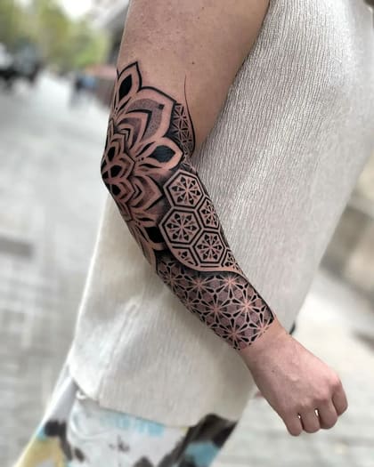 Tatuagem de manga geométrica com mandala e padrões hexagonais em dotwork no braço de uma pessoa.