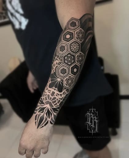 Tatuagem de manga geométrica masculina em blackwork e pontilhismo, com padrões de hexágonos e mandalas no braço.