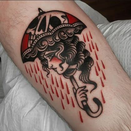 Tatuagem Old School de mulher com guarda-chuva de caveira e chuva vermelha no braço, estilo tradicional.