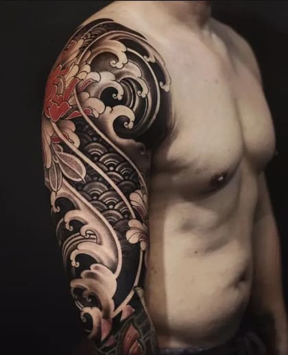 Tatuagem de braço estilo Oriental com ondas e flores vermelhas e brancas em fundo preto.