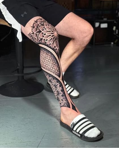 Tatuagem de perna completa masculina em estilo pontilhismo e blackwork, com design de mandala e padrões geométricos detalhados.