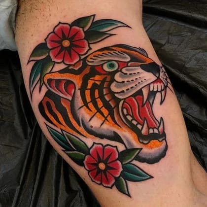 Tatuagem de tigre rugindo em estilo Old School com flores vermelhas e folhas verdes, cores vibrantes e traços marcantes.