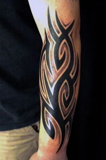 Tatuagem tribal preta e cinza no antebraço de um homem, com padrões abstratos e linhas fluidas.
