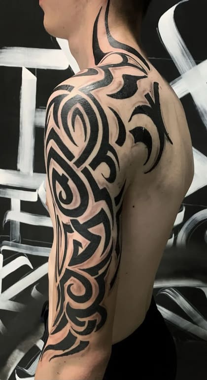 Tatuagem tribal preta e sólida cobrindo o ombro e braço de um homem, com padrões abstratos e fluidos.