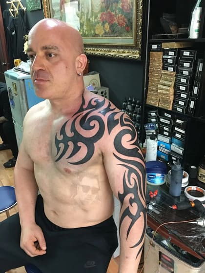 Homem com tatuagem tribal preta no ombro, braço e peito, em estúdio de tatuagem no Brasil.