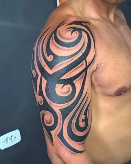 Tatuagem tribal blackwork no ombro de um homem, com padrões abstratos e sombreado.