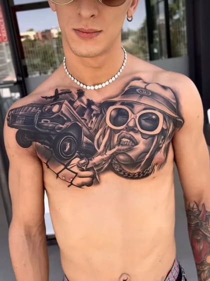 Tatuagem chicana detalhada no peito de um homem, com mulher de óculos e chapéu, carro lowrider e palmeiras em preto e cinza.